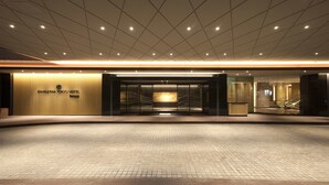 A hotel entrance with a modern design, featuring a reception desk, a glass door entrance, and a tiled floor.