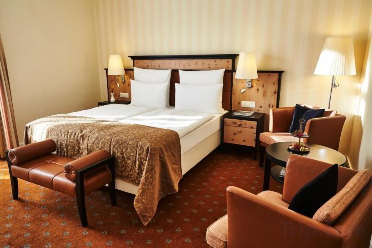 Habitación de hotel con cama doble, zona de estar con mesa y sillas, sofá y un pequeño escritorio con lámpara.