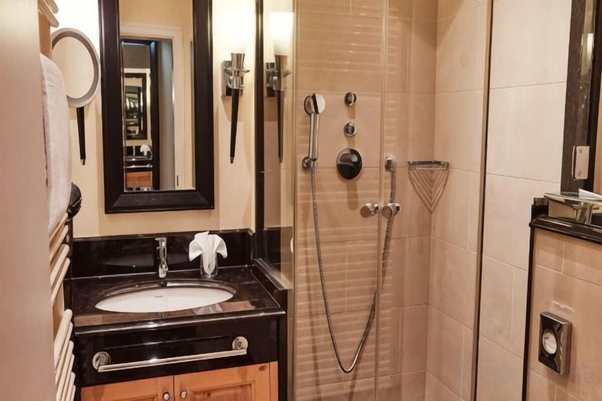 Een badkamer met een wastafel, spiegel, handdoekrek en een douche met een handdouche.