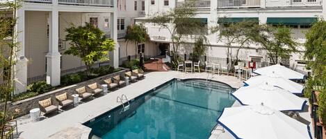 A pool area with lounge chairs and umbrellas, surrounded by multi-story buildings with balconies.