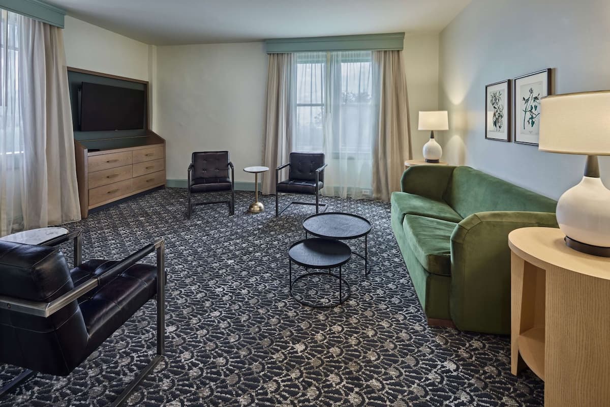 A hotel room with a sofa, two armchairs, a TV, a lamp, and a patterned carpet.