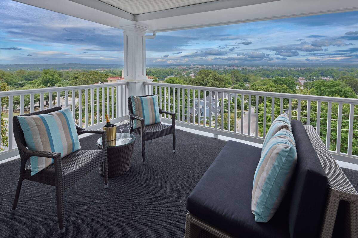 A covered balcony with wicker furniture, a glass table, and a view of a cityscape.