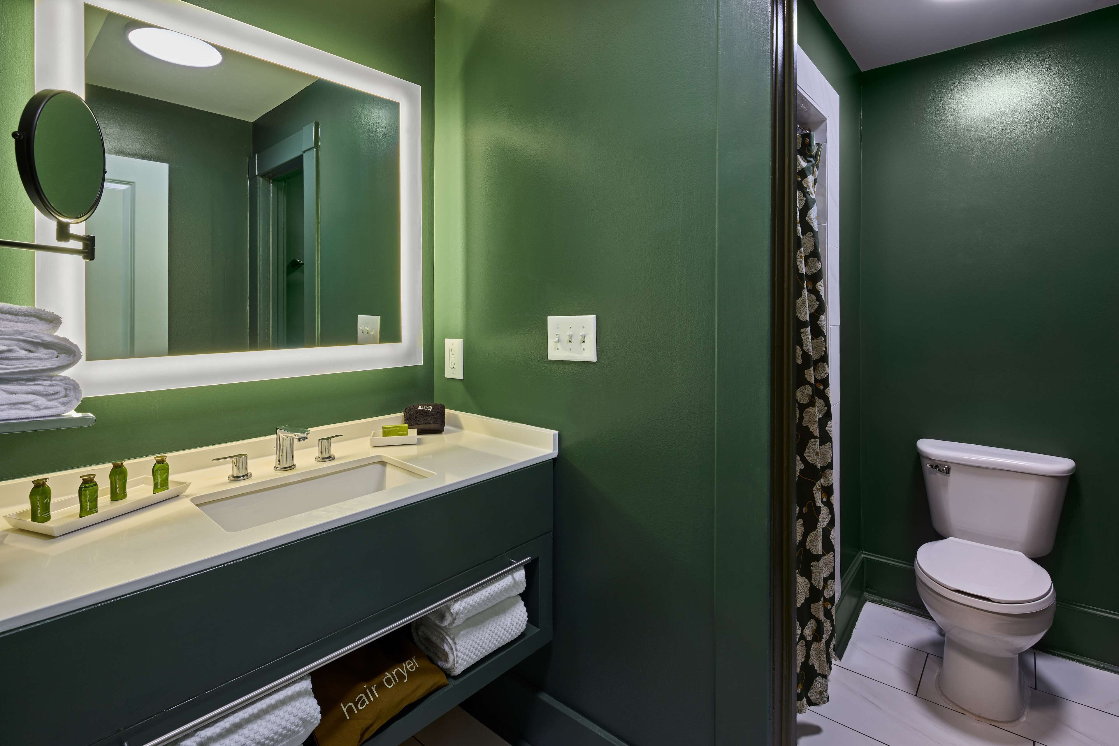A bathroom with a green wall, a white sink, a mirror, and a toilet.