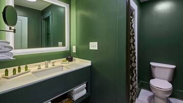 A bathroom with a green wall, a white sink, a mirror, and a toilet.