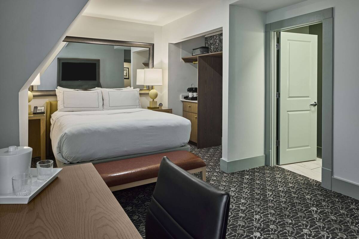 A hotel room with a bed, bedside table, lamp, and a small seating area.