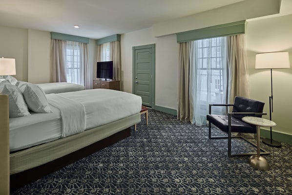 A hotel room with a large bed, a desk, a chair, and a TV.