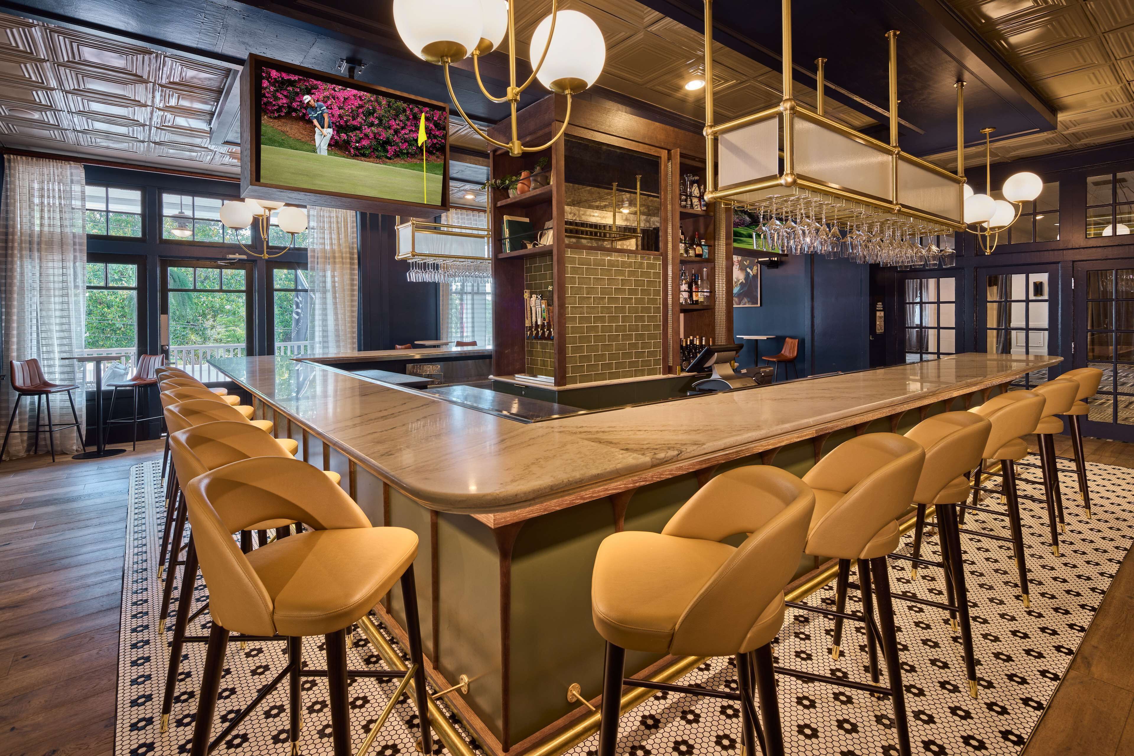 A bar area with a long counter, multiple stools, and a modern chandelier.