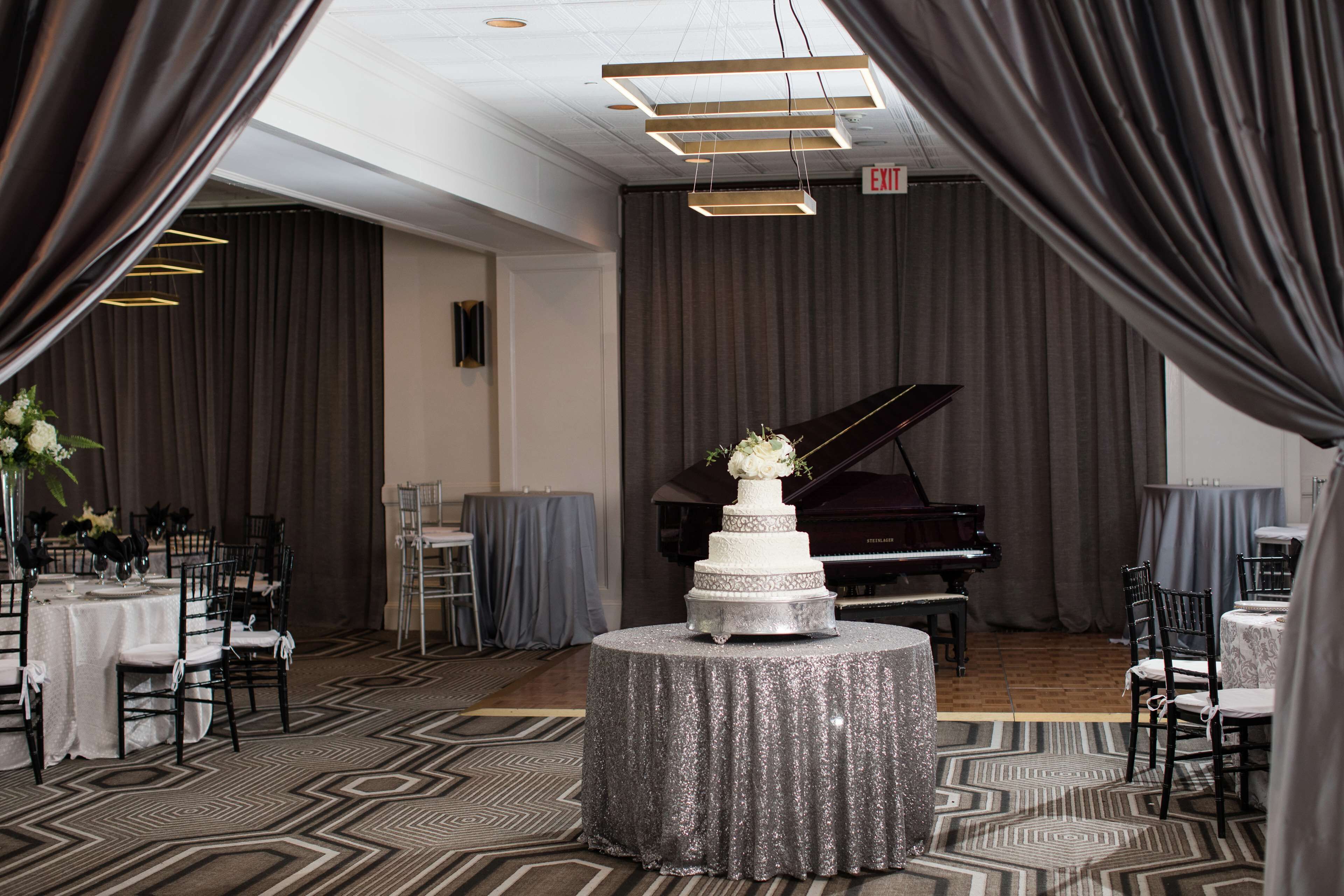 Un espace événementiel élégant, doté d’un grand piano, d’un gâteau à trois étages posé sur une table ronde et d’un tapis à motifs.