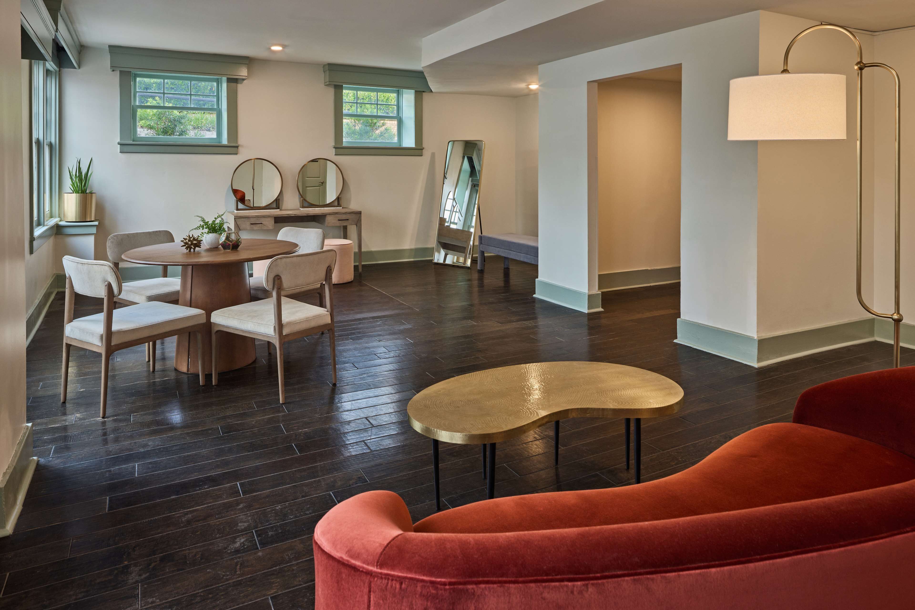 A spacious room with a wooden floor, a red sofa, a round table, and a dining area with chairs and a small table.