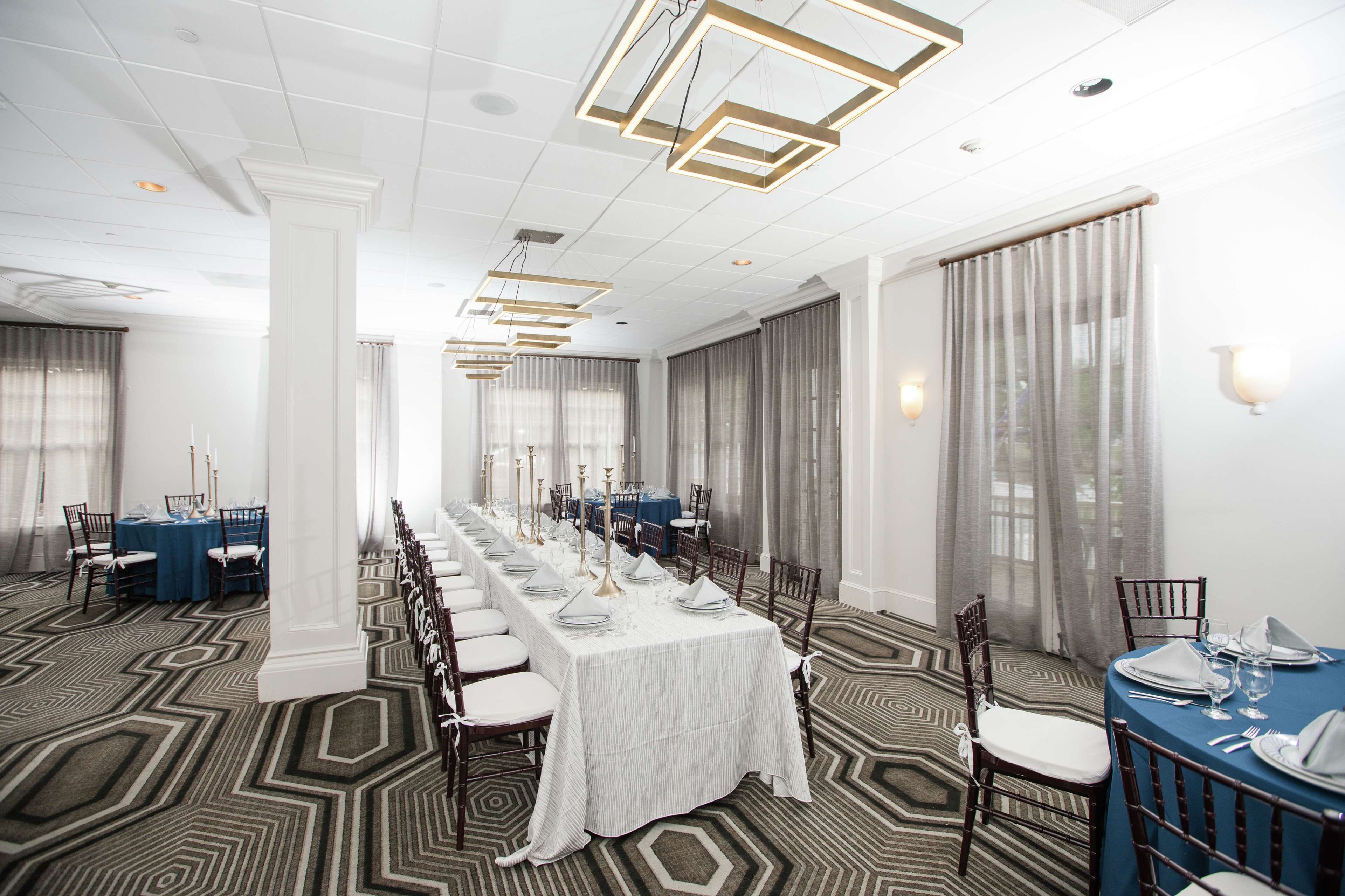 A long dining table set with white tablecloths, blue table runners, and dark chairs.