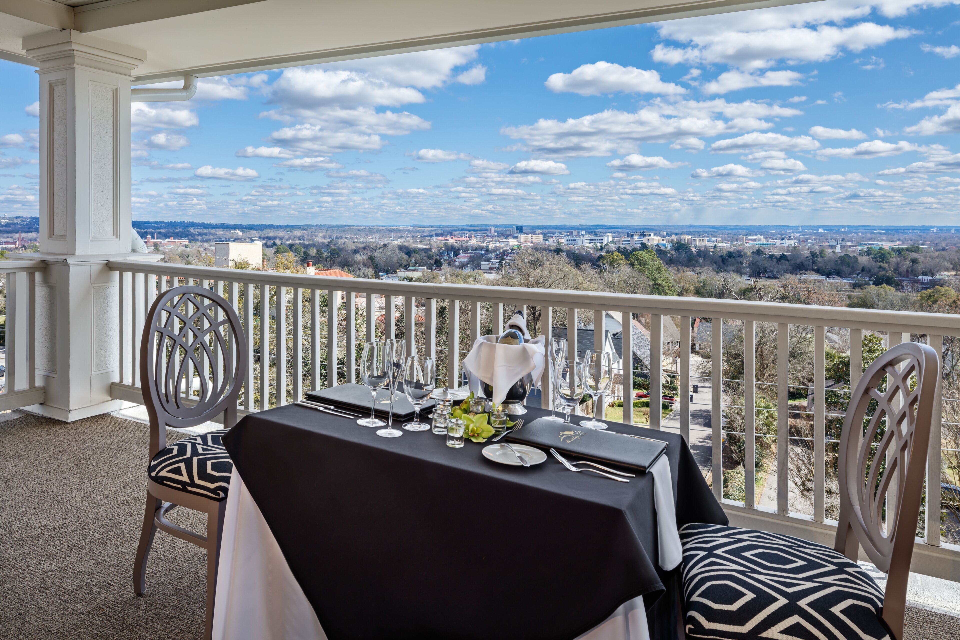 A balcony with a table set for dining, overlooking a cityscape.