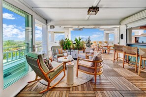 A spacious outdoor deck with wooden flooring, comfortable seating, and large windows offering a view of the city.