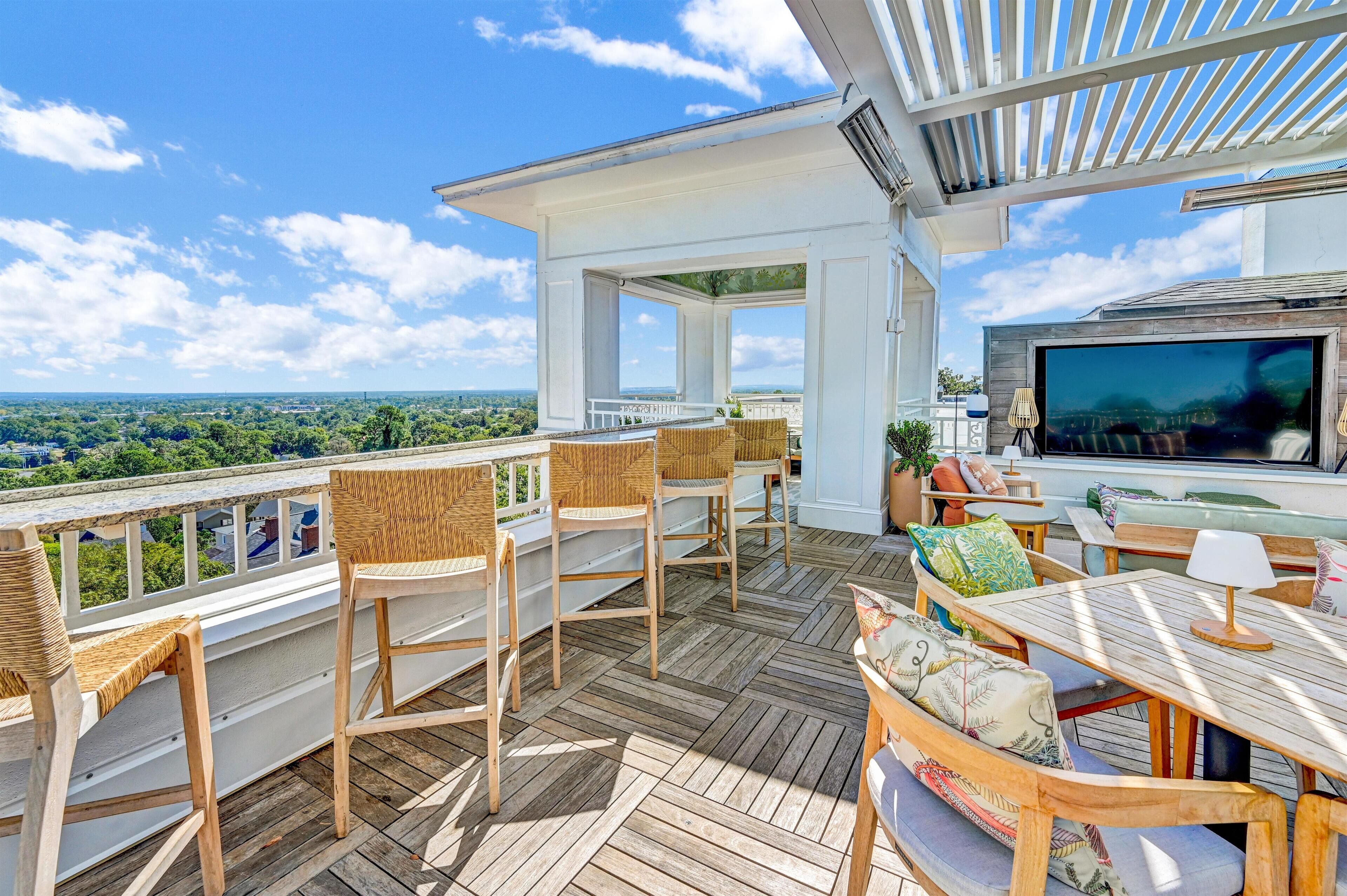 A wooden deck with wicker chairs and a table, overlooking a scenic landscape.