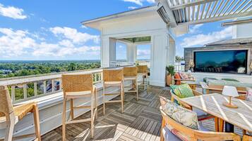 A wooden deck with wicker chairs and a table, overlooking a scenic landscape.