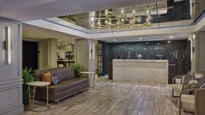 A spacious lobby with a modern reception desk, a comfortable seating area with a sofa and chairs, and a decorative ceiling light fixture. - The Partridge Inn Augusta, Curio Collection by Hilton (Augusta)