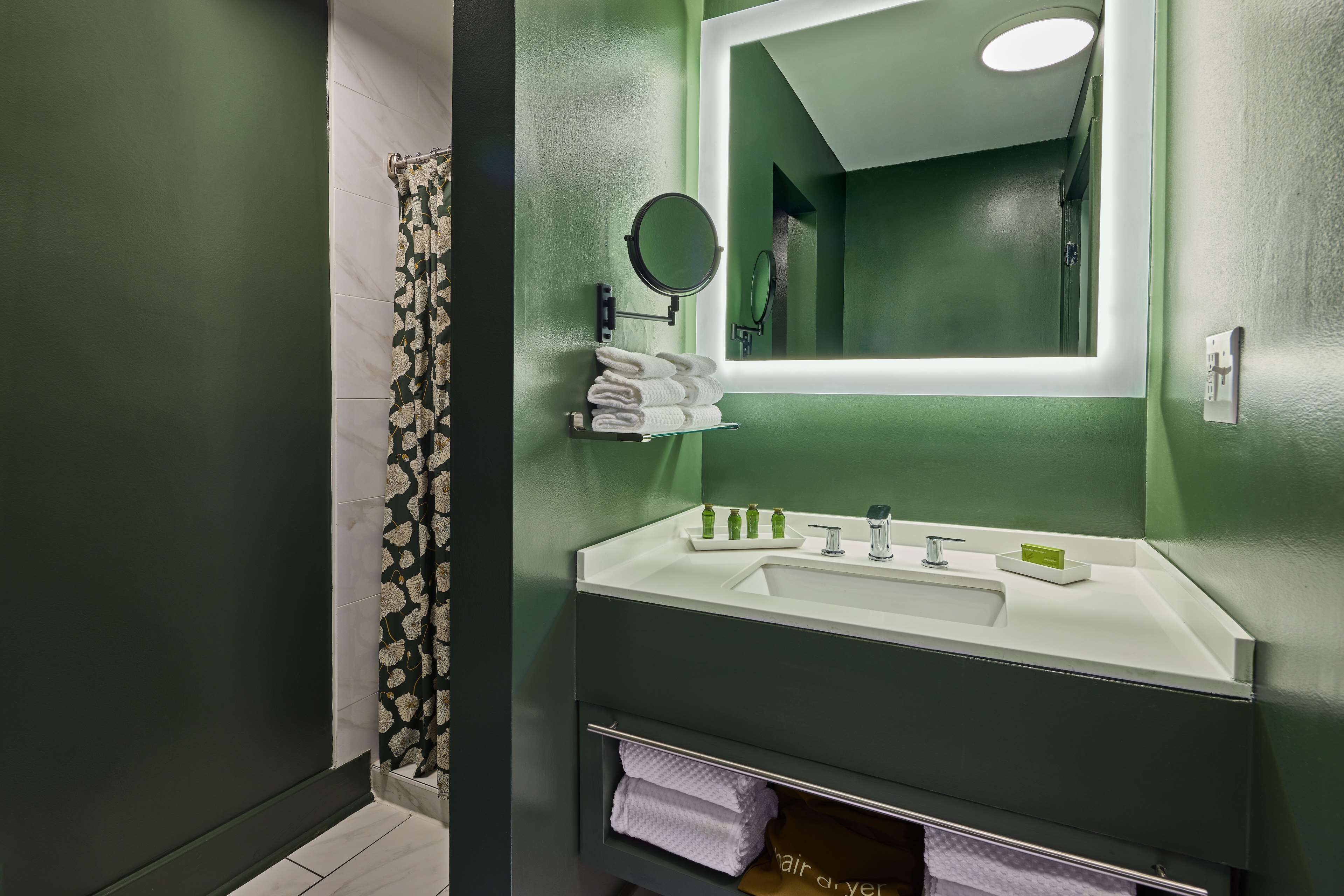 A bathroom with a green wall, a white sink, a mirror, and a towel rack.