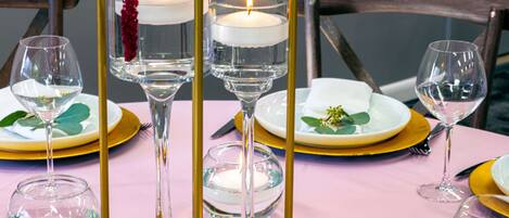 Una mesa dispuesta con platos dorados y blancos, copas transparentes y velas en candelabros.
