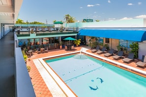 A hotel with a swimming pool, outdoor seating, and a view of the city.