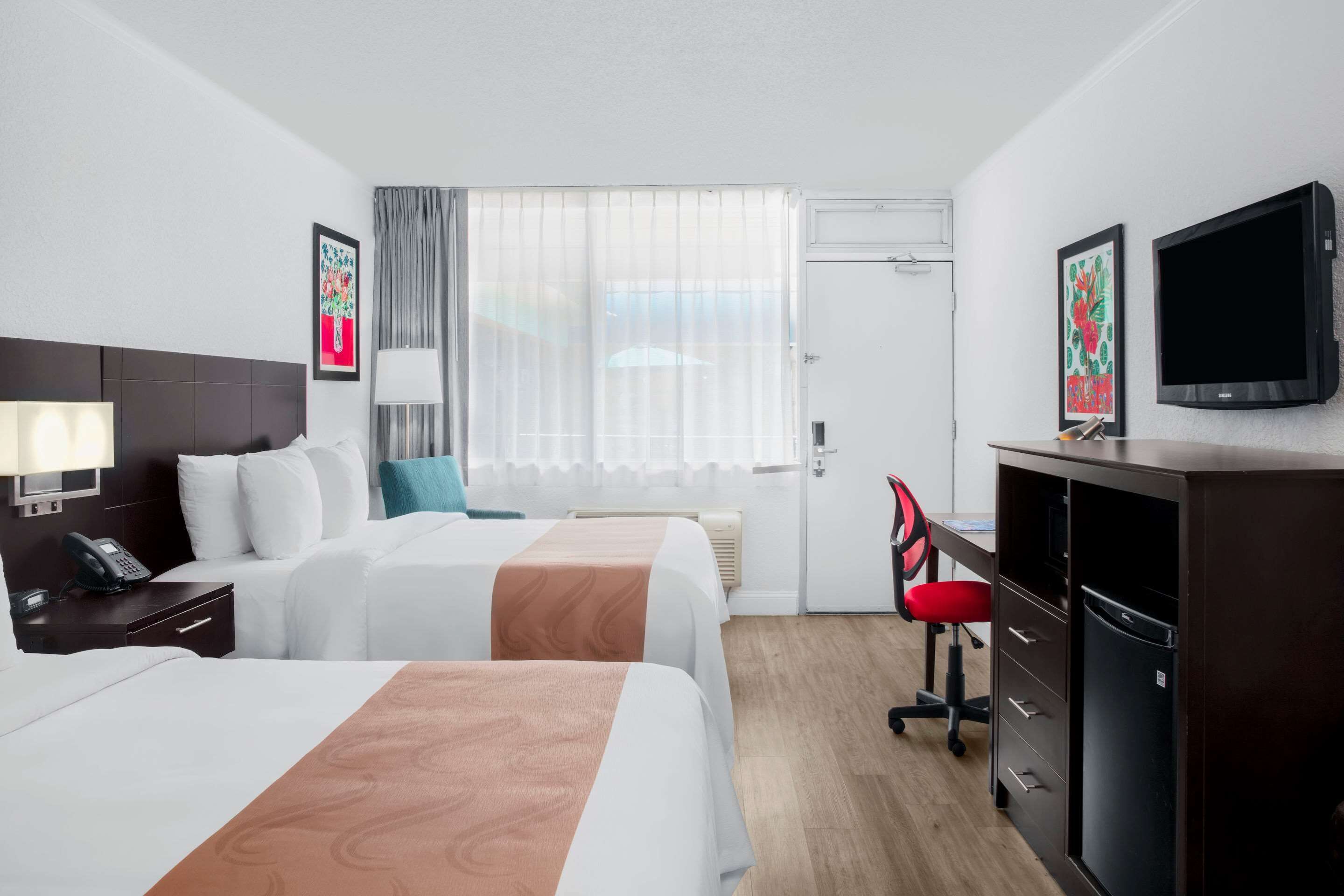 Een hotelkamer met twee bedden, een bureau, een stoel, een televisie en een minibar.