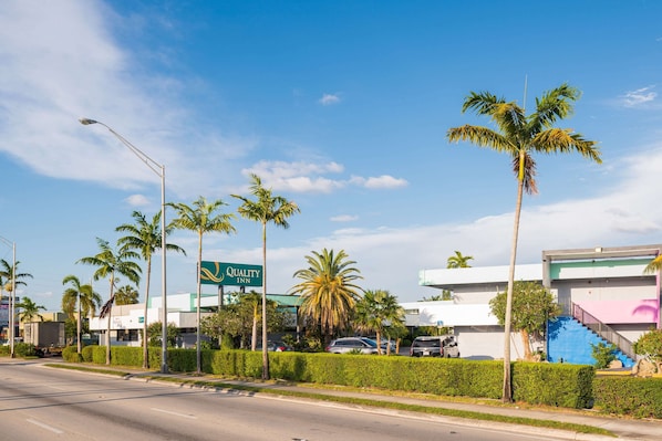 A Quality Inn hotel with a clear view of the road, palm trees, and a blue staircase.