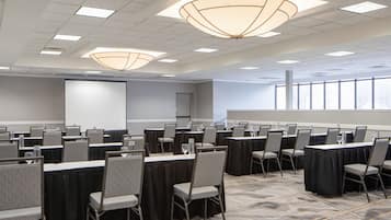 A conference room with rows of tables and chairs, a projector screen, and large windows.