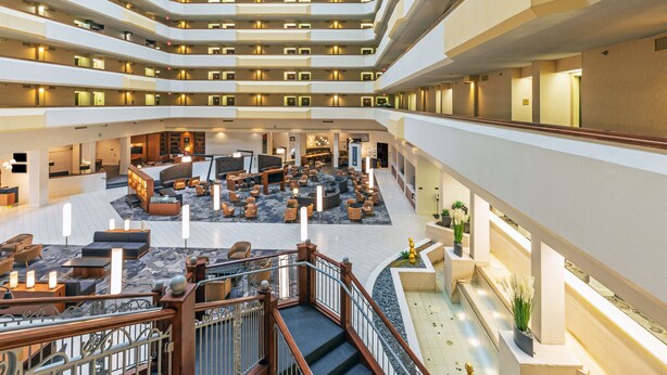 Un lobby de hotel de varios niveles con una zona de estar central y una escalera.