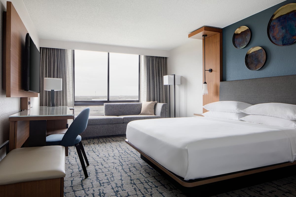 A hotel room with a bed, desk, chair, and a large window offering a view.