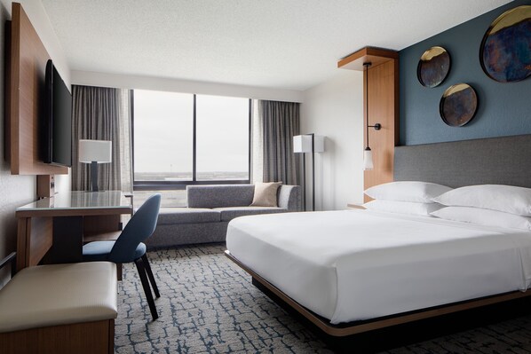 A hotel room with a bed, desk, chair, and a large window offering a view. - Houston Marriott South at Hobby Airport (Houston)