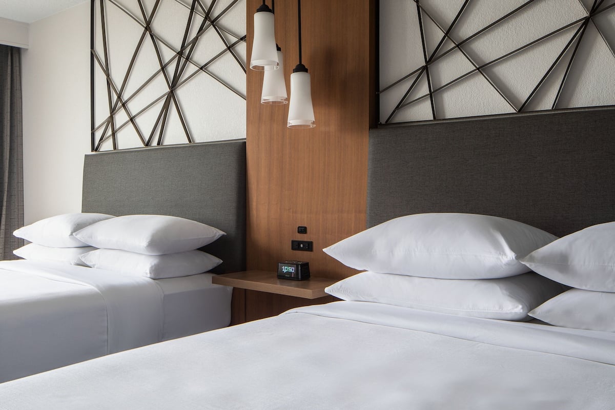 A hotel room with two beds, a wooden headboard, a nightstand with a clock, and geometric wall decor.