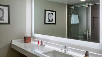 A modern bathroom with a large mirror, two sinks, and a glass-enclosed shower.