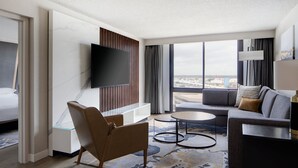 Una habitación de hotel moderna con un televisor grande, un sofá, una silla y vistas a la ciudad.