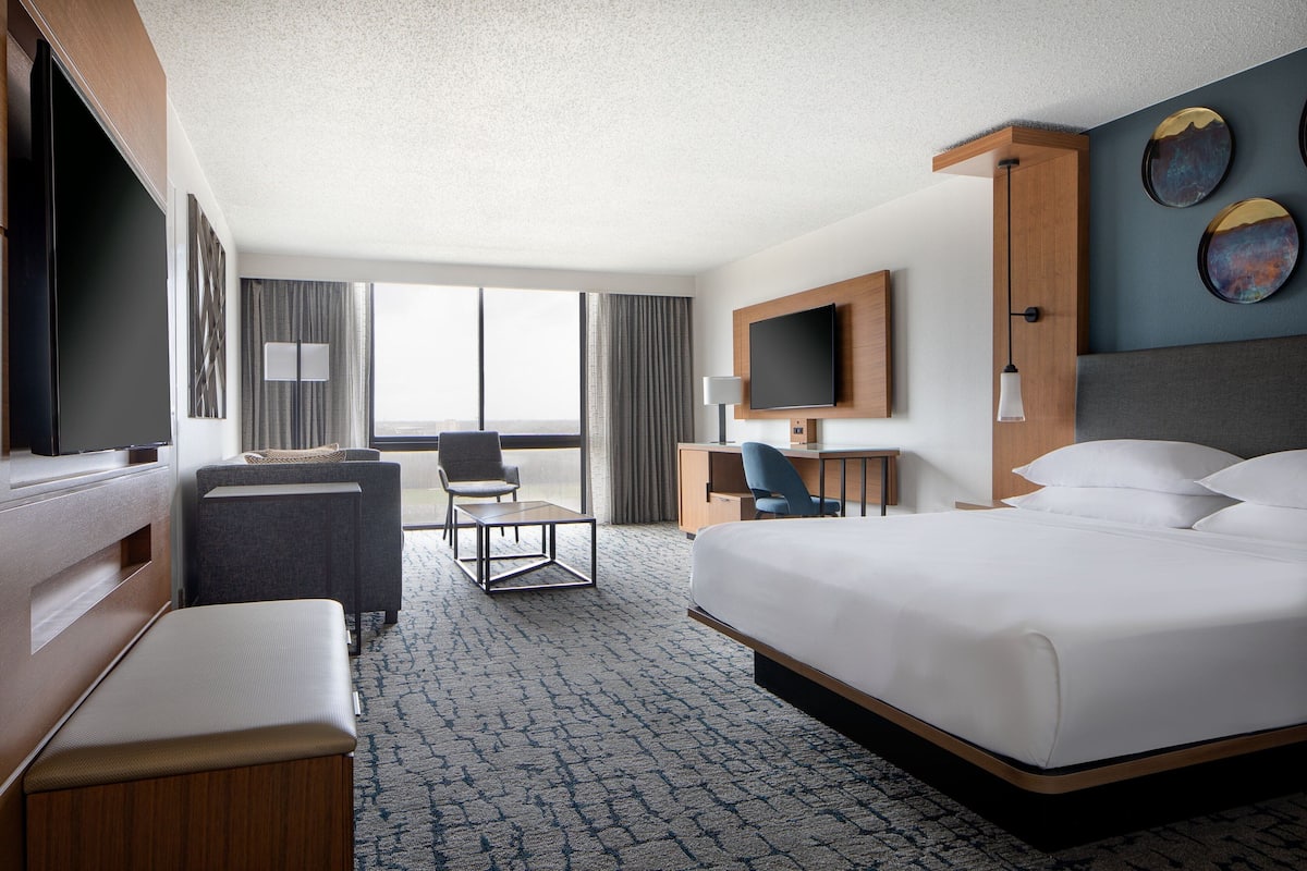 A hotel room with a large bed, a desk, a chair, a TV, and a view of the outdoors.