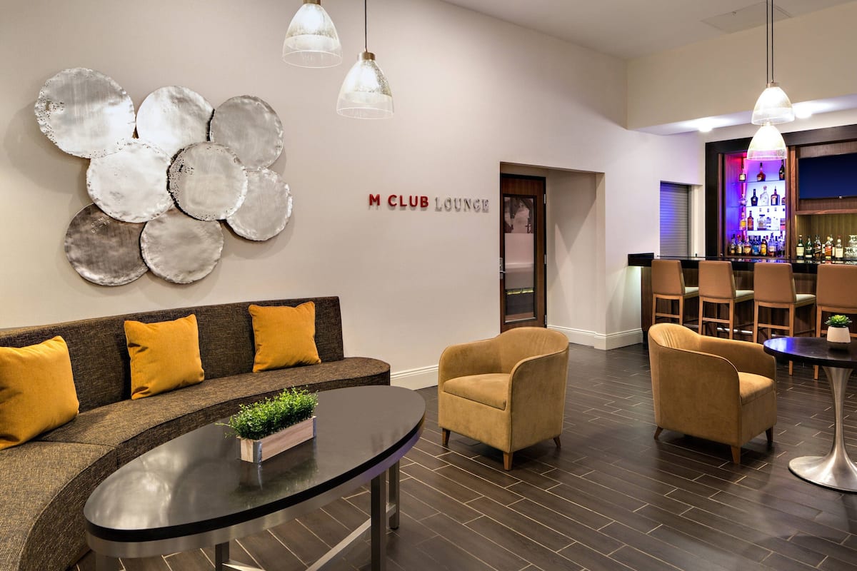 A modern lounge area with a sofa, armchairs, a coffee table, and a bar with shelves of bottles.