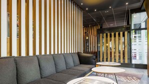 A modern lobby with a grey sofa, two round tables, and a striped wooden wall. - B&B Hotel Düsseldorf-Hbf (Düsseldorf)