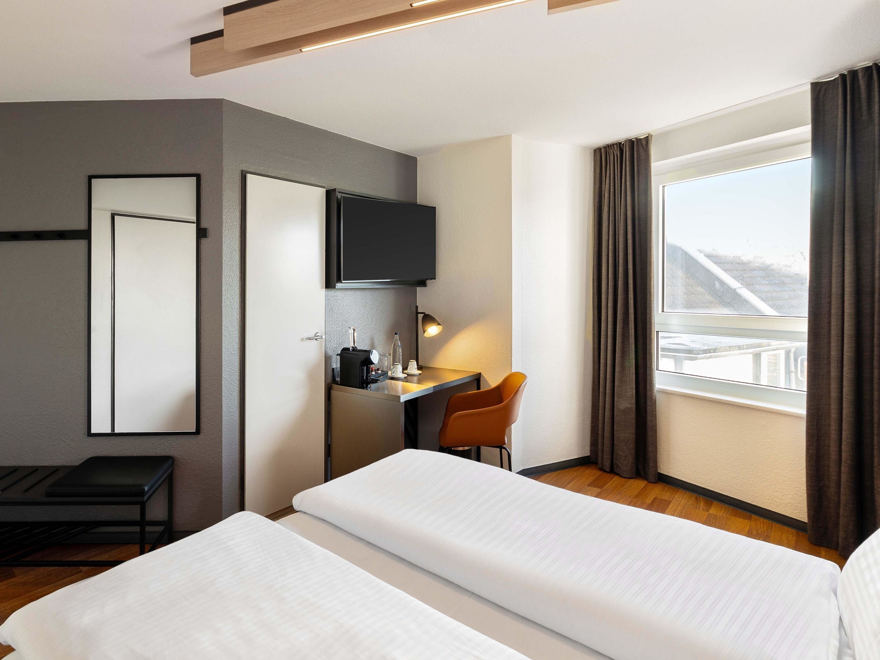 Una habitación de hotel con dos camas, un escritorio con silla, televisor y ventana con cortinas.