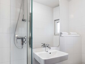 Un baño moderno con ducha de vidrio, un lavabo blanco y un espejo que refleja una ventana y toallas.