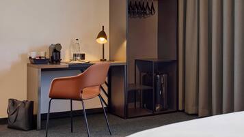 Habitación de hotel con escritorio, silla, cama y vestidor con ropa colgada.
