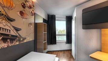 Une chambre d’hôtel moderne, équipée d’un lit, d’une télévision, d’une fenêtre avec des rideaux et d’un mur au décor traditionnel.