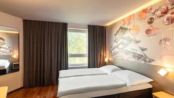 Habitación de hotel con una cama, ventana con cortinas, lámpara de pared y un mural decorativo.