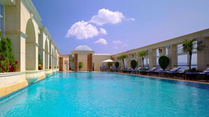 A large swimming pool with lounge chairs and umbrellas, surrounded by a building with columns and a dome structure.