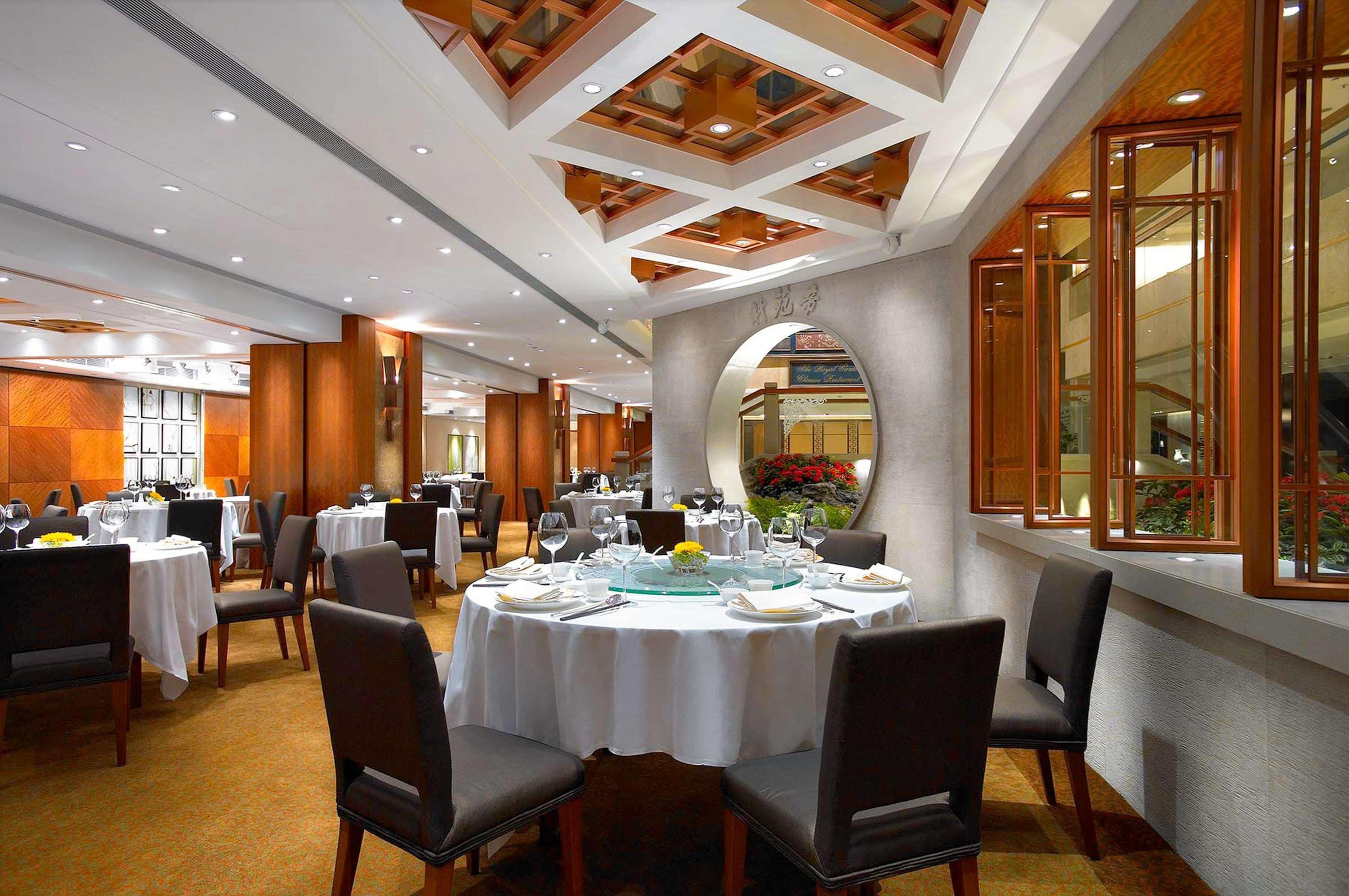 A well-lit dining area with round tables, chairs, and a large window with a view.
