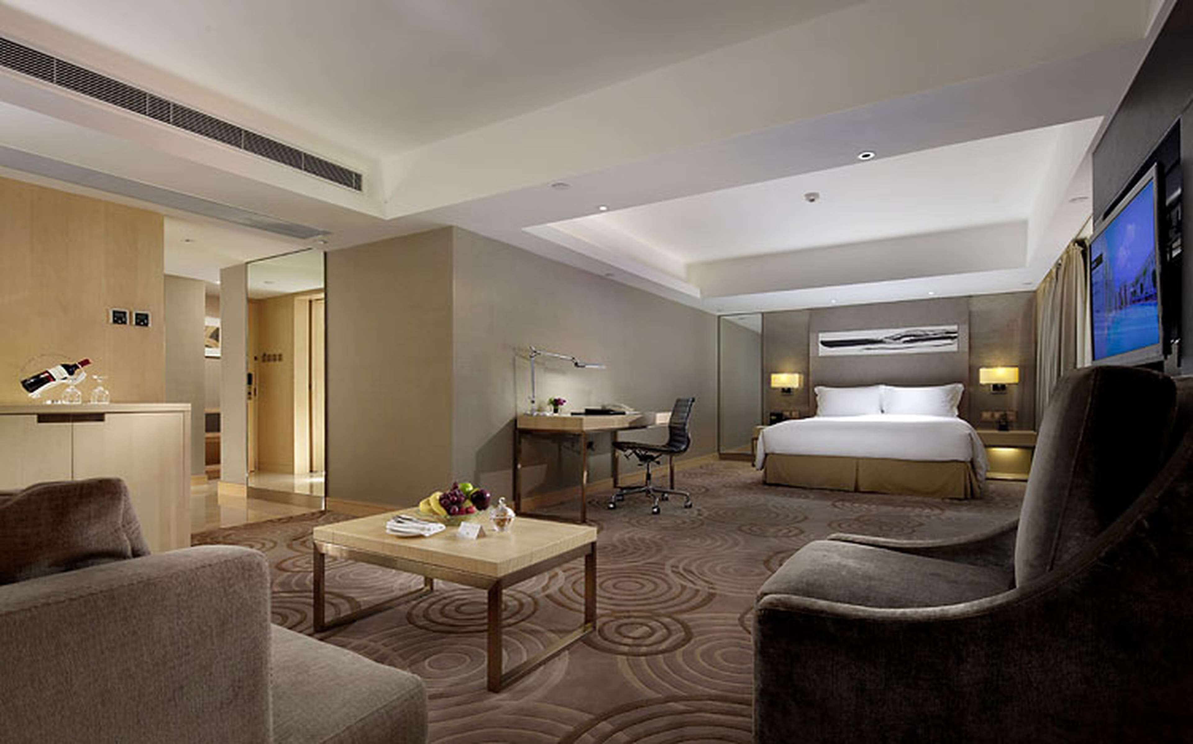 A modern hotel room with a bed, a desk, a chair, a coffee table, and a TV.