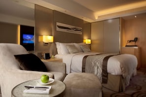 A hotel room with a bed, two bedside tables, a chair, a round table with a plate and utensils, and a television in the background.