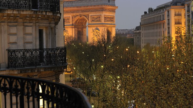 Une vue de l’Arc de Triomphe à Paris, entouré d’arbres et d’immeubles.
