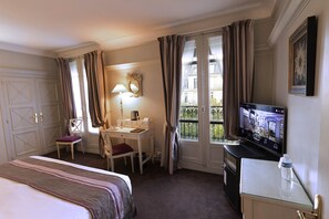 Een hotelkamer met een bed, bureau, stoel, televisie en een raam met gordijnen.