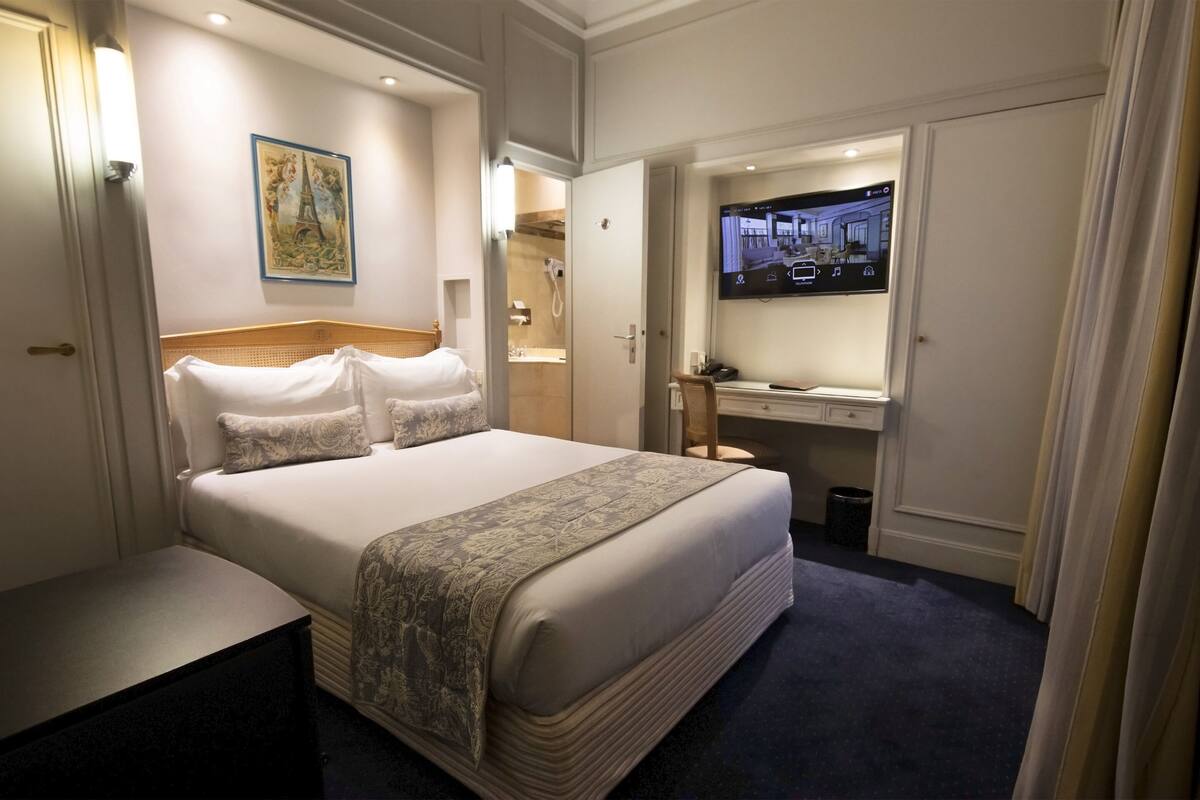 Une chambre d’hôtel avec un grand lit, une télévision, un bureau avec une chaise et une salle de bain visible à travers une porte ouverte.