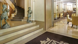 Une entrée imposante avec un escalier en marbre, un paillasson décoratif et un hall d’entrée bien éclairé qui mène à un espace salon.