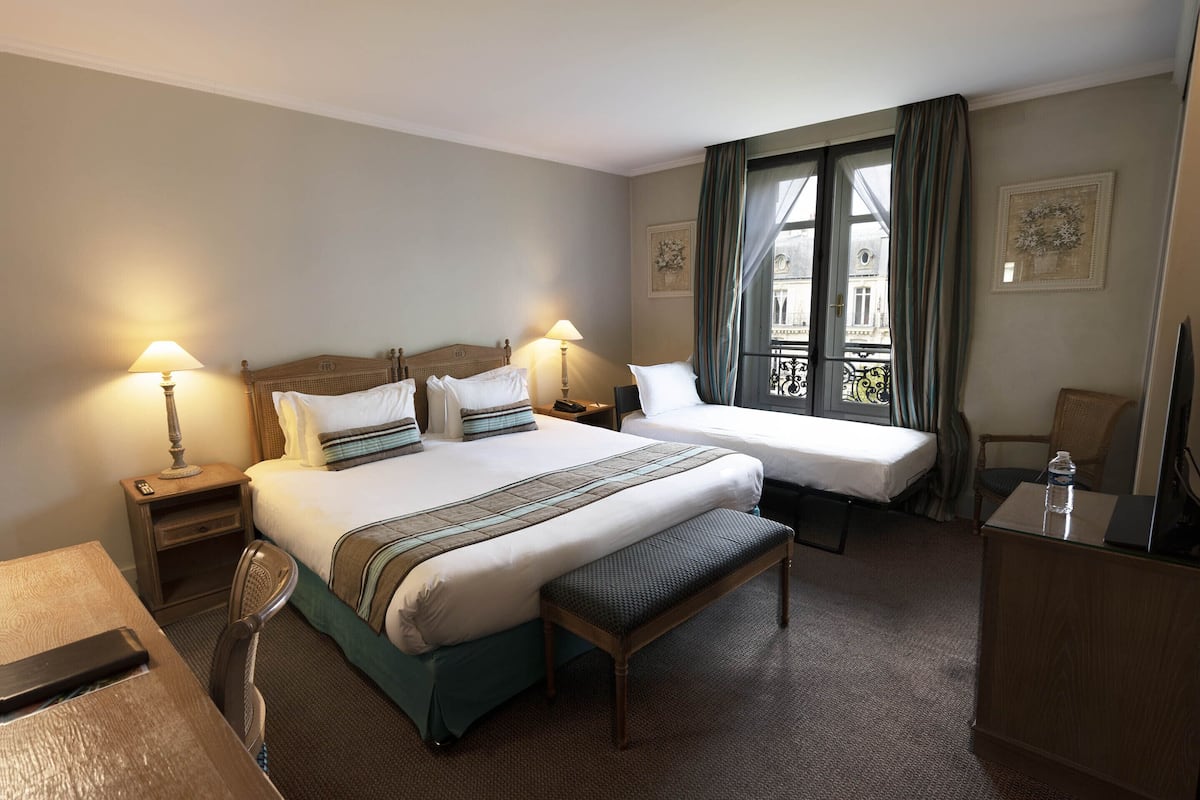 Une chambre d’hôtel avec deux lits, un bureau, une chaise, un banc et un téléviseur.