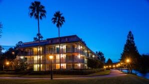 Een meerlaags gebouw met balkons, omringd door verzorgde gazons en palmbomen, wat wijst op een resort- of hotelomgeving.
