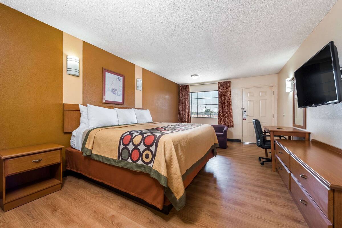 Habitación de hotel con cama, escritorio, silla, televisor y ventana con cortinas.